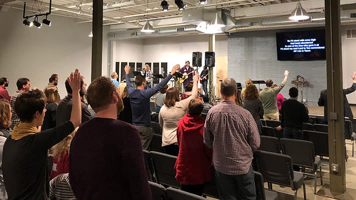 Congregation worshiping at Antioch Community Church in Minneapolis with hands raised in praise.