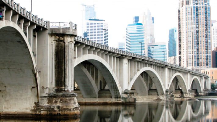 Historic stone bridge over the Mississippi River with the Minneapolis skyline in the background.