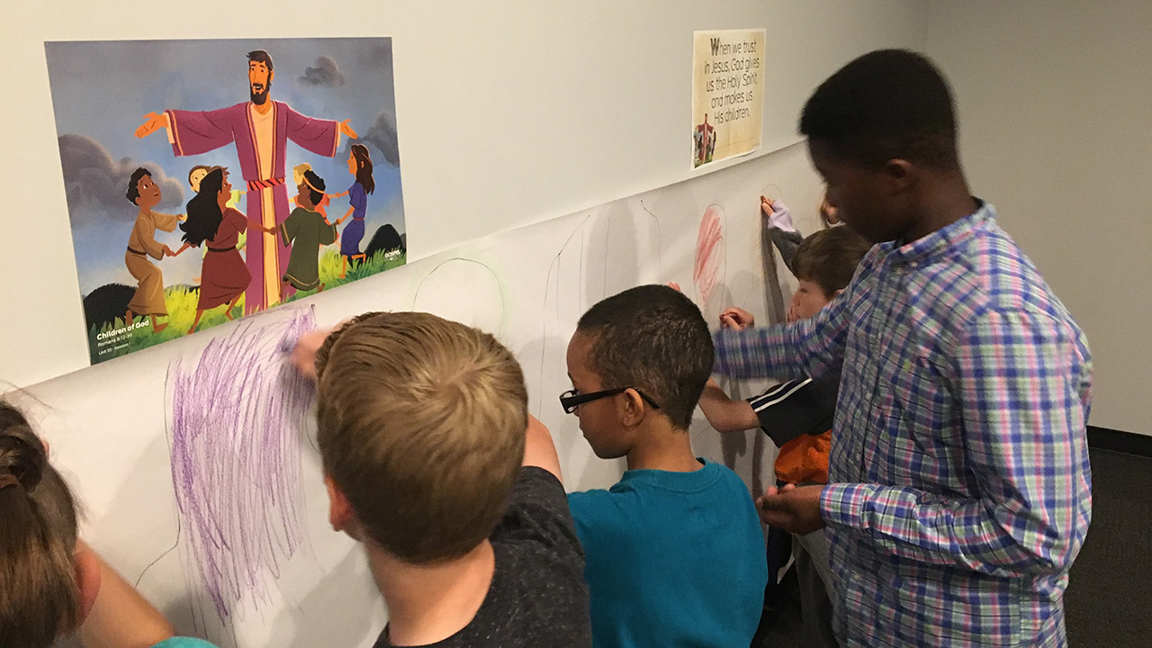 Children at Antioch Community Church in Minneapolis engaging in a creative Bible lesson, drawing on a mural with an illustration of Jesus and children in the background.