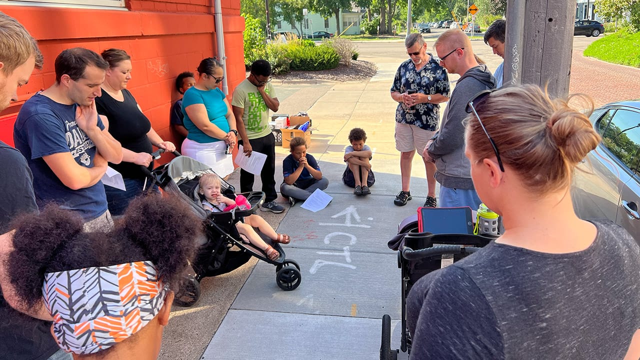 Antioch Community Church members praying together on a Minneapolis sidewalk during a community outreach event.